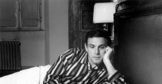 A man in a striped shirt sleeping in bed.