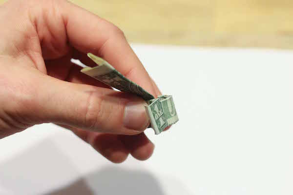 Folding vertical section of dollar bill down by hand.  