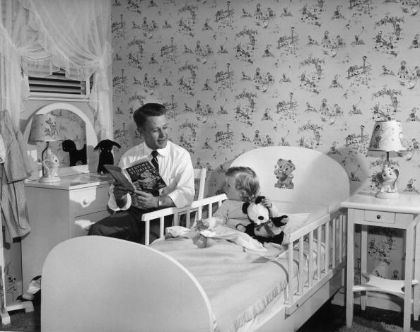 Vintage dad looking at his child while reading book.