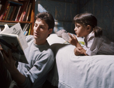 A man and a girl reading a book in bed.