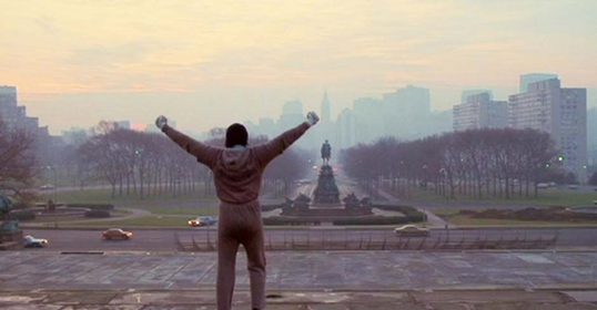 A man with his arms raised in the air in front of a city after completing his training.
