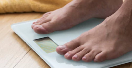 A person's feet on a scale, monitoring their weight loss journey.