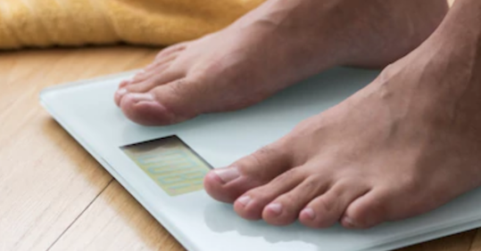 A person's feet on a scale, monitoring their weight loss journey.