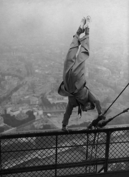 Vintage man doing handstand on railing while high up in the air.
