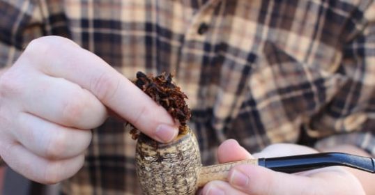 A person holding a tobacco pipe with a piece of tobacco packed in it.