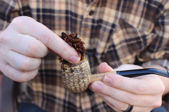 A person holding a tobacco pipe with a piece of tobacco packed in it.