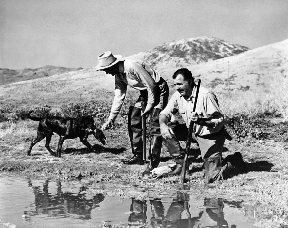 Vintage hunters with dog and carrying the guns on a river side.