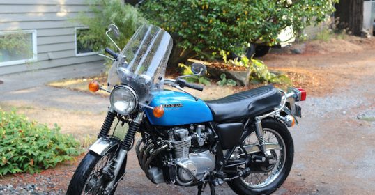 A blue motorcycle parked on a driveway next to a house.