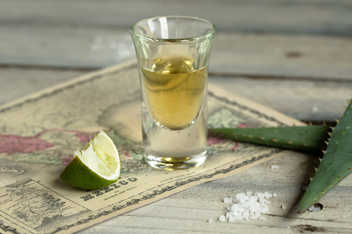 Tequila displayed with a used lemon and a solution in a glass.