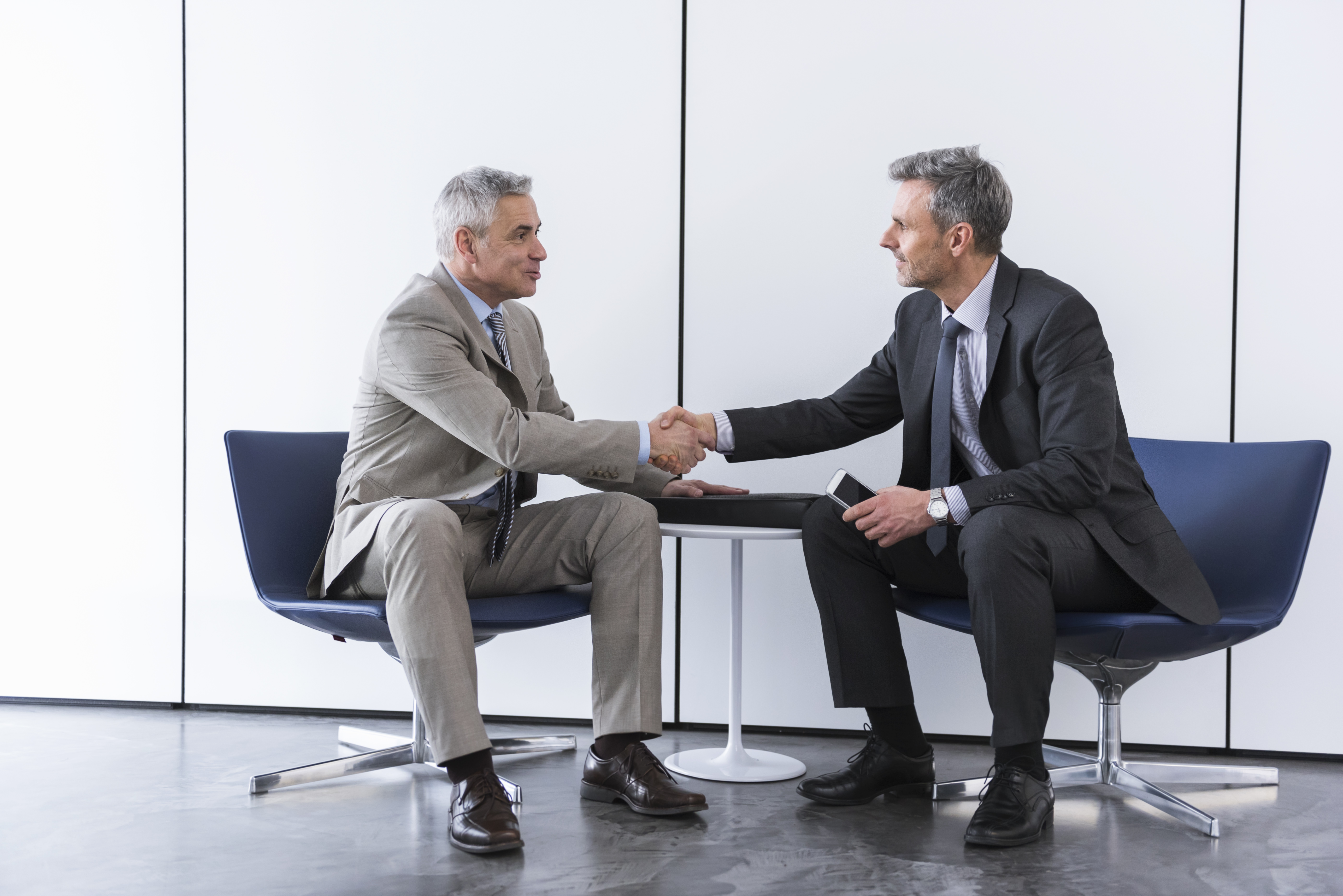 Two businessmen in formal dress shaking hands during negotiations in an office.