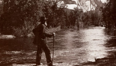 An old photograph of a man standing by a river, capturing the beauty of nature.