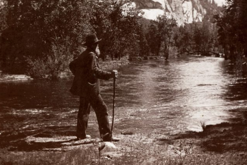 An old photograph of a man standing by a river, capturing the beauty of nature.