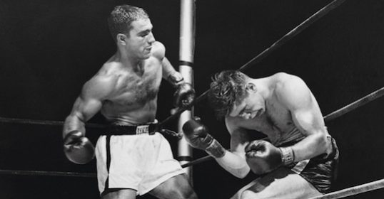 A black and white photograph of two boxers in a boxing ring, captured during a intense fight.