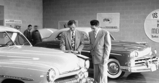 Two men negotiating a car deal in a showroom.
