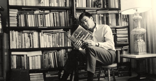 A man, famous for his martial arts skills, sits in a chair engrossed in a book.