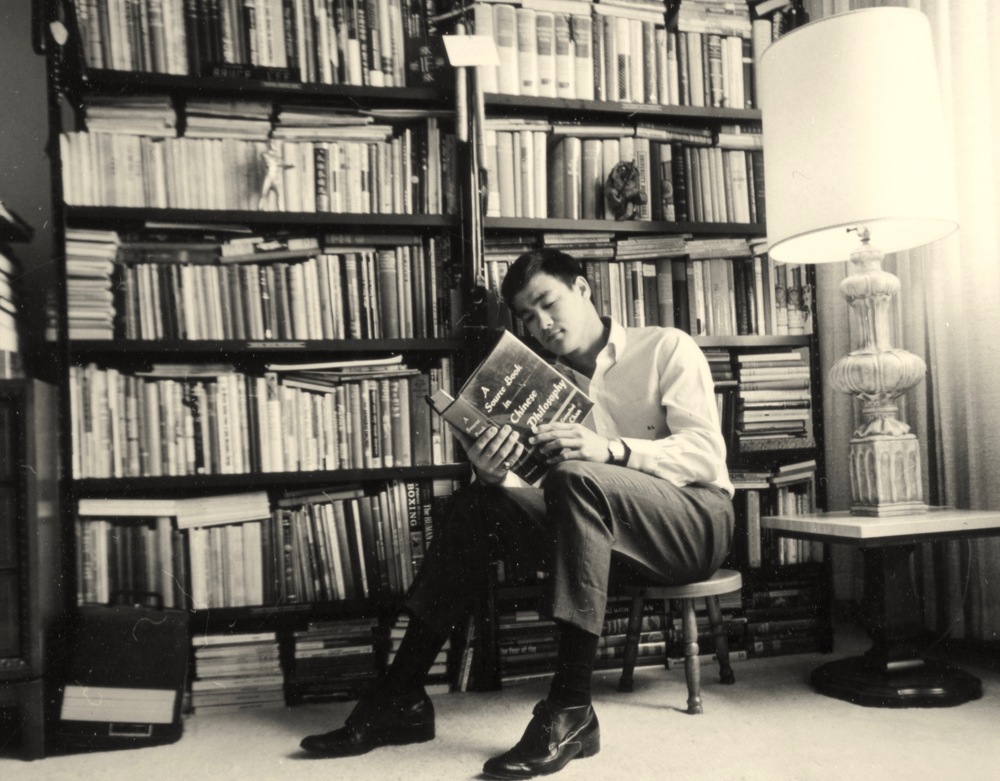 Formal dressed young man reading the life of Bruce Lee in a library.