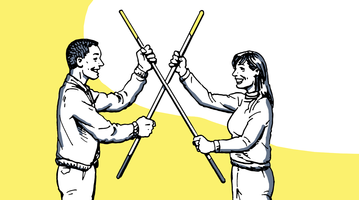 A man and his partner stand holding sticks in front of a yellow background.