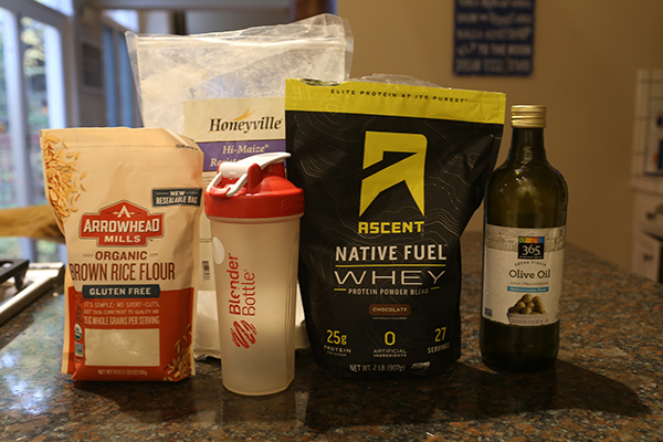 Protein powder, Blender bottle, brown rice, flour and olive oil displayed.
