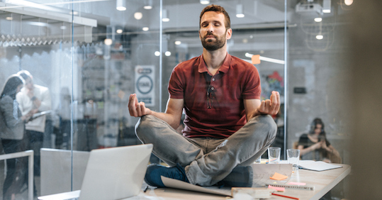 A man meditating at his desk in an office.