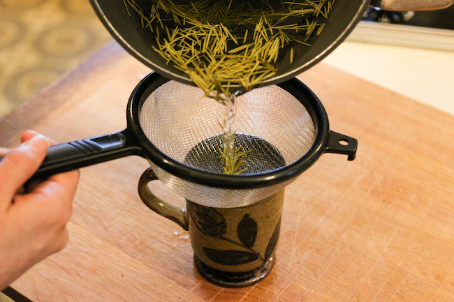 Filtering Douglas fir after boiling in water with strainer.