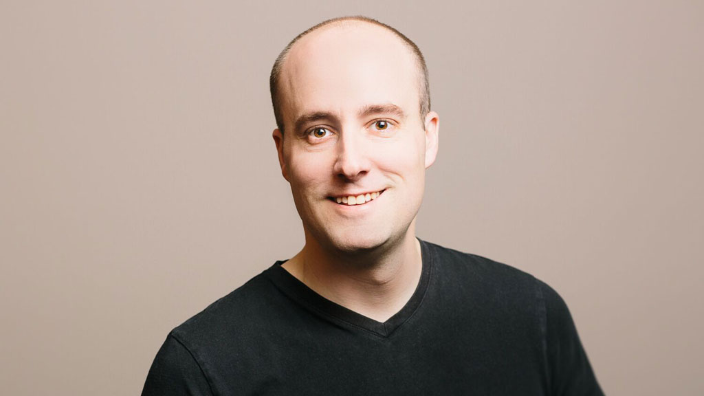 A bald man in a black v-neck shirt smiles while discussing mental models on his podcast.