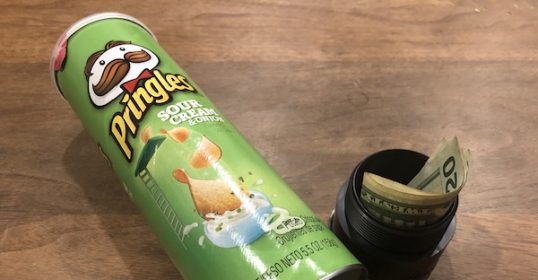 A can of potato chips sits beside a can of money.