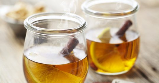 Two jars of hot tea with lemon slices and playing cards on a wooden table, perfect for a cold night.