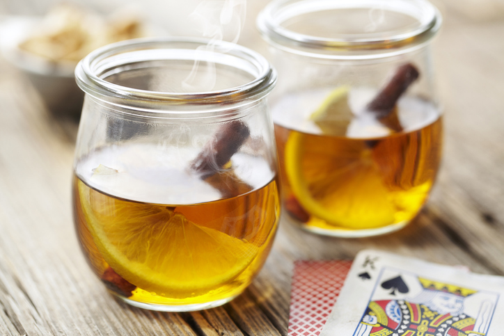 Two jars of hot tea with lemon slices and playing cards on a wooden table, perfect for a cold night.