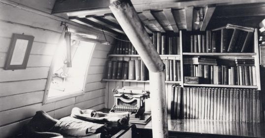 A vintage black and white photo of a room filled with books and a typewriter.