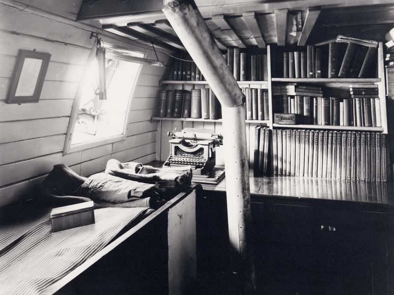 A vintage black and white photo of a room filled with books and a typewriter.