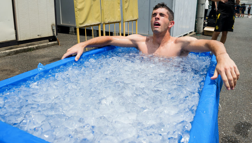 A man is sitting in a tub of ice for exercise recovery.