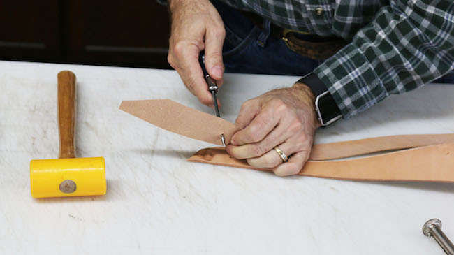 Pinching hole in leather strip and a hammer is placed.