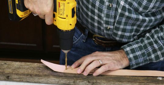 A man using a drill on a piece of wood.
