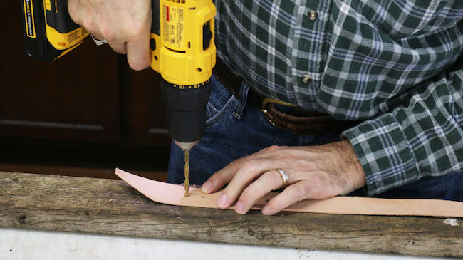 Man using power drill on a leather strip.