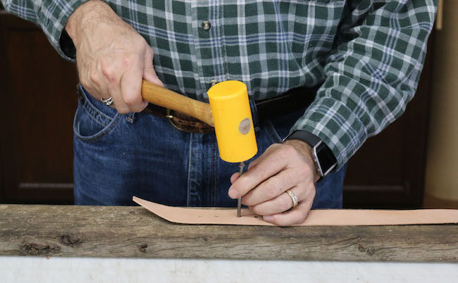 Punching leather with nail by hammer.