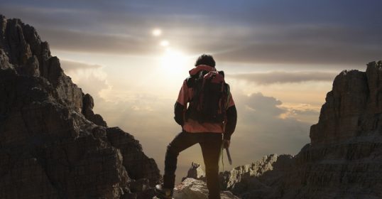 A man is standing on top of a mountain at sunset, reflecting on the beauty of nature.