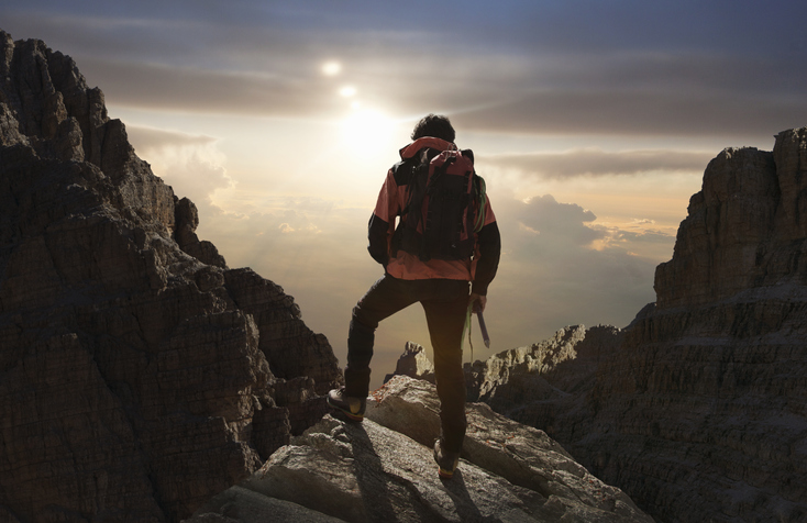 A man is standing on top of a mountain at sunset, reflecting on the beauty of nature.