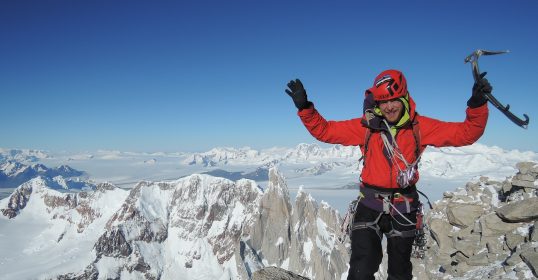 A climber standing on top of a mountain with his arms raised in celebration.