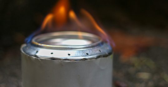 A soda can stove siting on the ground with a flame.