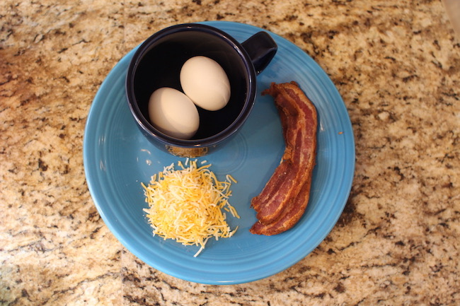 Two eggs in cup along with cheese and sausage displayed in plate.