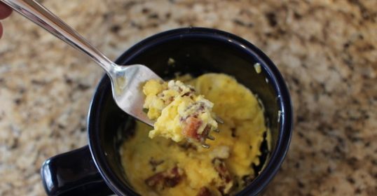 A person is holding an incredible spoonful of eggs in a mug.