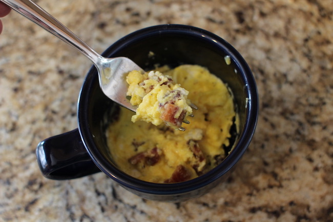 Paste of scrambled egg with cheese and sausage taken out of cup with folk.