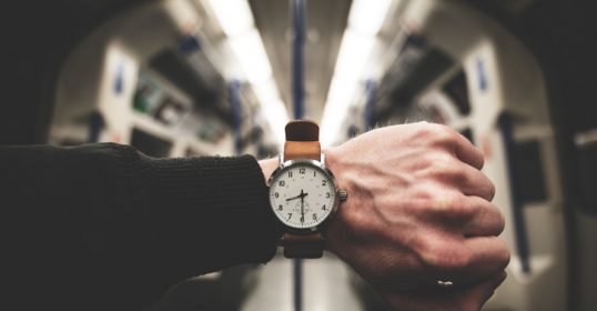 A man's hand on a train with a watch, keeping track of time.