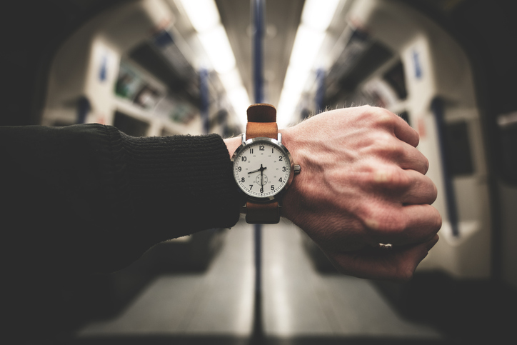 A man's hand on a train with a watch, keeping track of time.