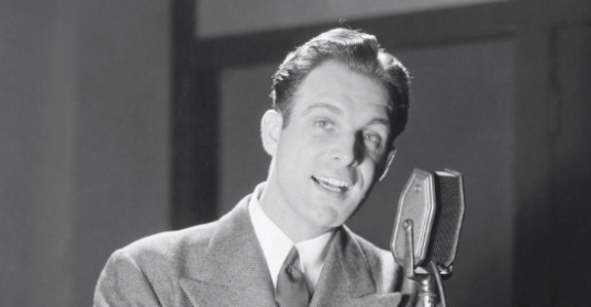 A man in a suit is speaking into a microphone to improve his podcast.
