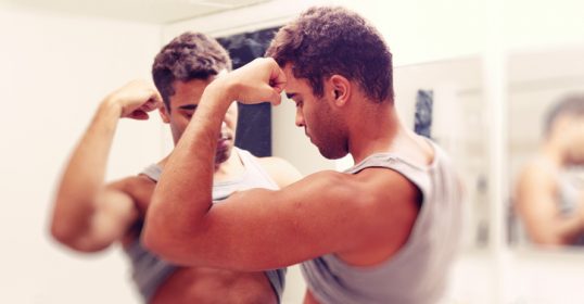 A man with male body image issues standing in front of a mirror, experiencing bigorexia.