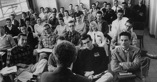 A black and white photo capturing a group of people in a classroom.