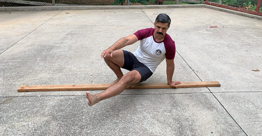 A man balancing on a 2x4 in a parking lot.