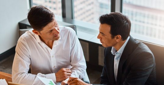 Two bosses discussing at a table in an office.