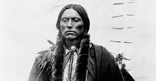 A black and white photo of an Indian tribe member holding a feather.